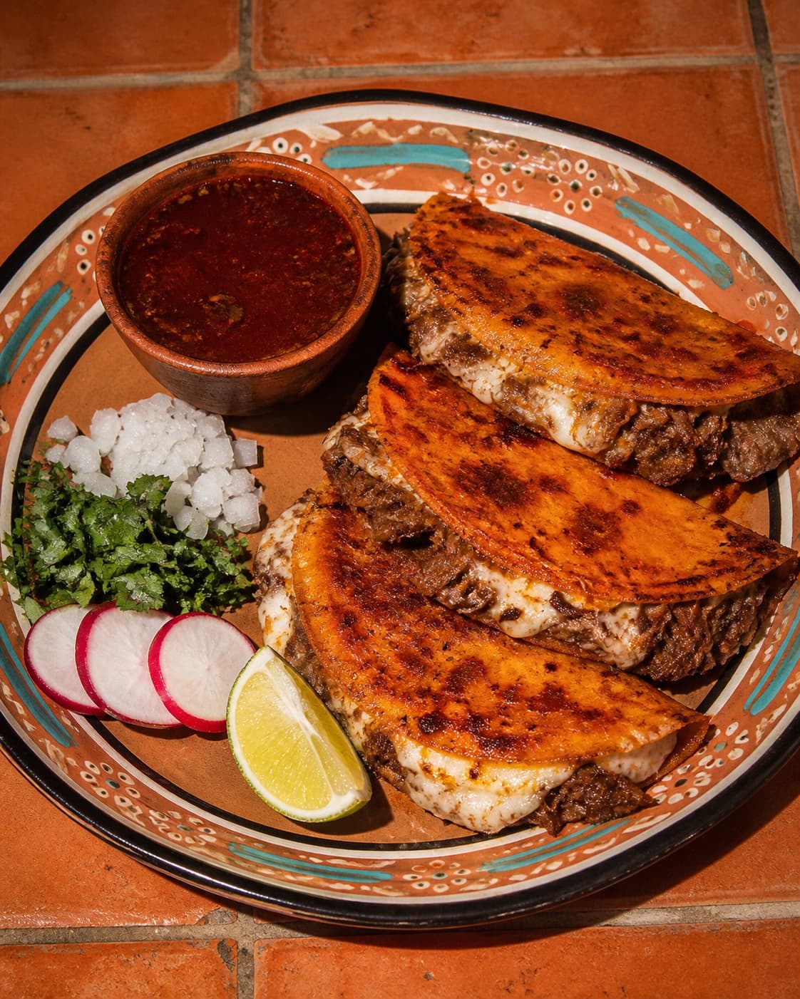 Three crisp quesa birria tacos with consommé, onion, cilantro, radish, and lime